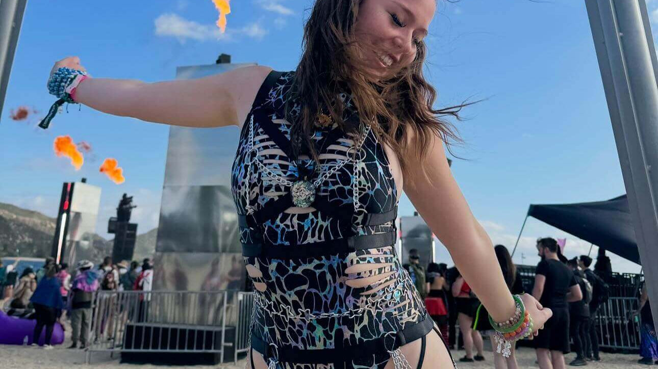 Woman dancing in a stylish rave outfit with flames in the background at a festival.