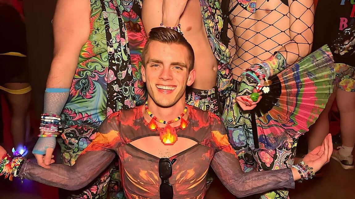 A group of festival-goers in vibrant men's rave clothes, featuring colorful patterns and fishnet tops, poses confidently in a lively club setting