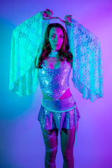 Woman in sparkly rave outfit with lace sleeves under vibrant purple lighting.