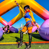 Woman in vibrant rave outfit striking a pose at a festival under colorful inflatable arches.
