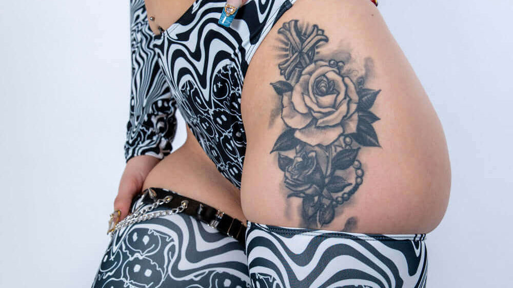 Close-up of a person in stylish black and white rave outfit showcasing intricate tattoo on leg.