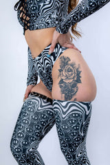 Close-up of a person in stylish black and white rave outfit showcasing intricate tattoo on leg.