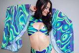 Model wearing a psychedelic patterned cape and bikini set from the Fantasia Rave Outfit Collection, featuring bold swirls of blue, green, and purple, embodying the spirit of rave fashion by Freedom Rave Wear.