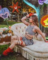 A girl wearing a black and white geometric printed crop top with black criss cross straps and a matching skirt. She is posing on a couch at a music festival.