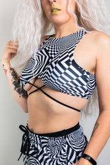 A girl wearing a black and white geometric printed crop top with black criss cross straps and matching pants.