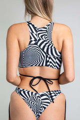 A girl wearing a black and white geometric printed crop top with black straps and matching bikini bottoms. She is facing away from the camera.