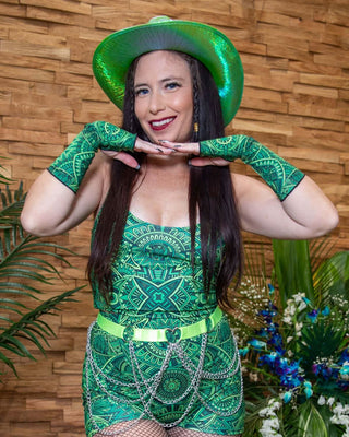 Young woman in green rave outfit and Dominion Gloves, posing with a vibrant hat and playful energy.