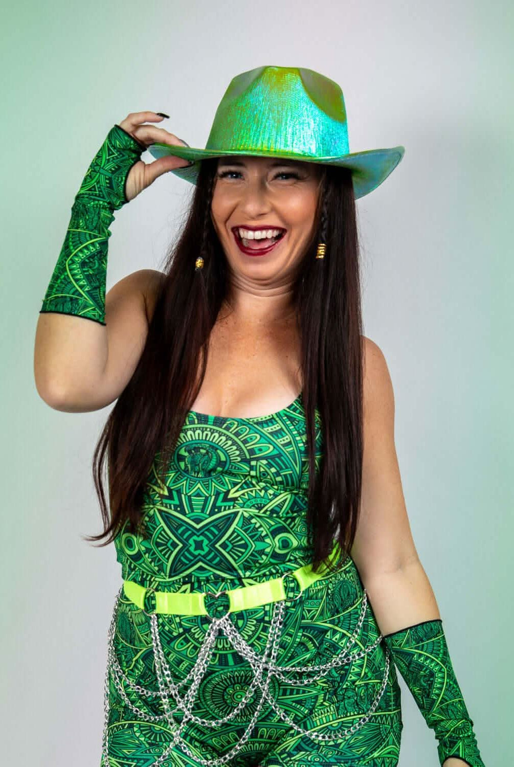 Woman in vibrant green rave outfit with a shiny hat, smiling energetically at the camera.