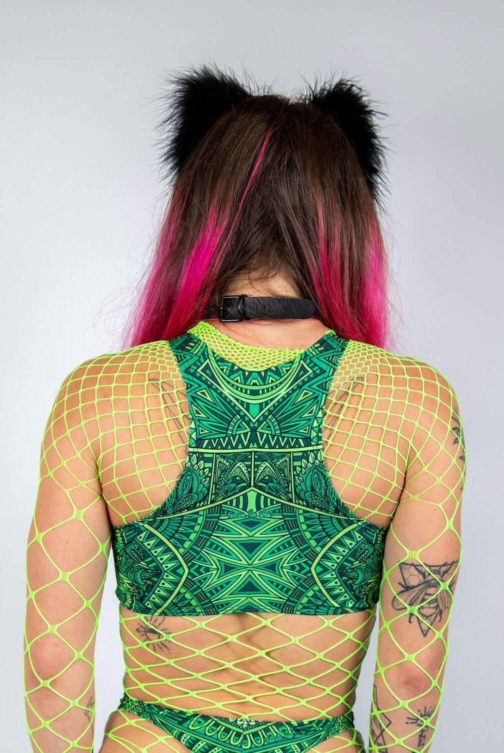 Back view of a model wearing a vibrant green rave top with fishnet detailing and cat ear accessories.