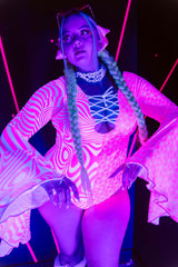 A woman standing in black light wearing a pink and white bodysuit with flowy sleeves that glows under the light.