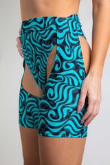 An up close photo of a woman wearing short chaps with a blue and black swirl design and matching bikini bottoms. She is facing to the left.