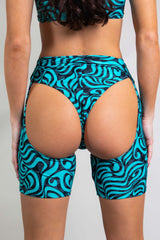 An up close photo of a woman wearing short chaps with a blue and black swirl design and matching bikini bottoms. She is facing away from the camera.