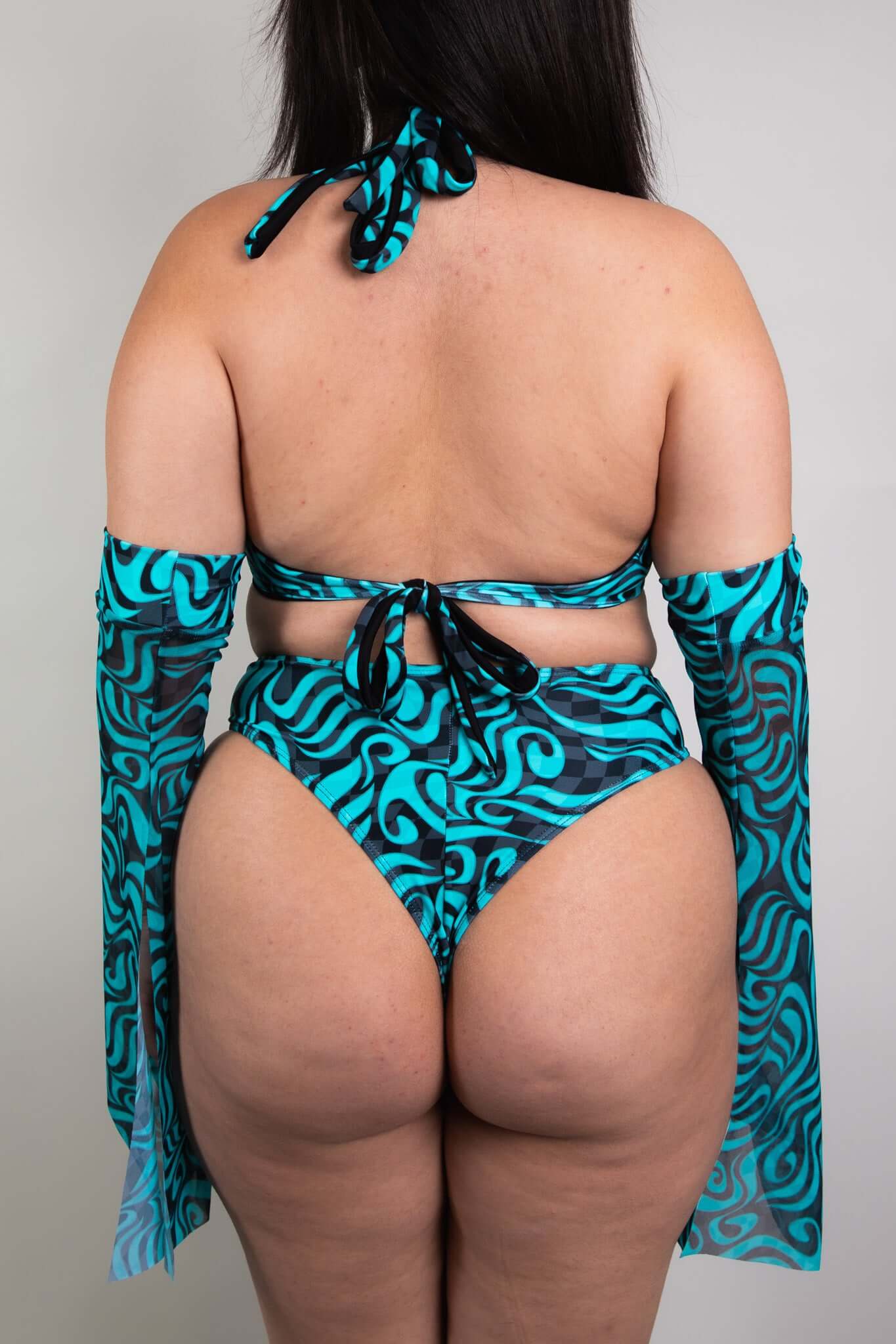 An up close photo of a woman wearing a blue and black swirled crop top and matching bikini bottoms. She is facing away from the camera.