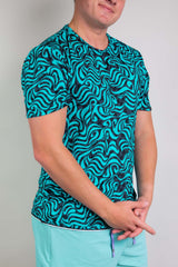 An up close photo of a man wearing a blue and black swirl printed t-shirt and light blue shorts.