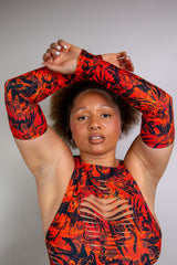 Front view of a model wearing a Freedom Rave Wear bodysuit, featuring bold orange and black arm sleeves with dynamic flame patterns, posed with arms raised.