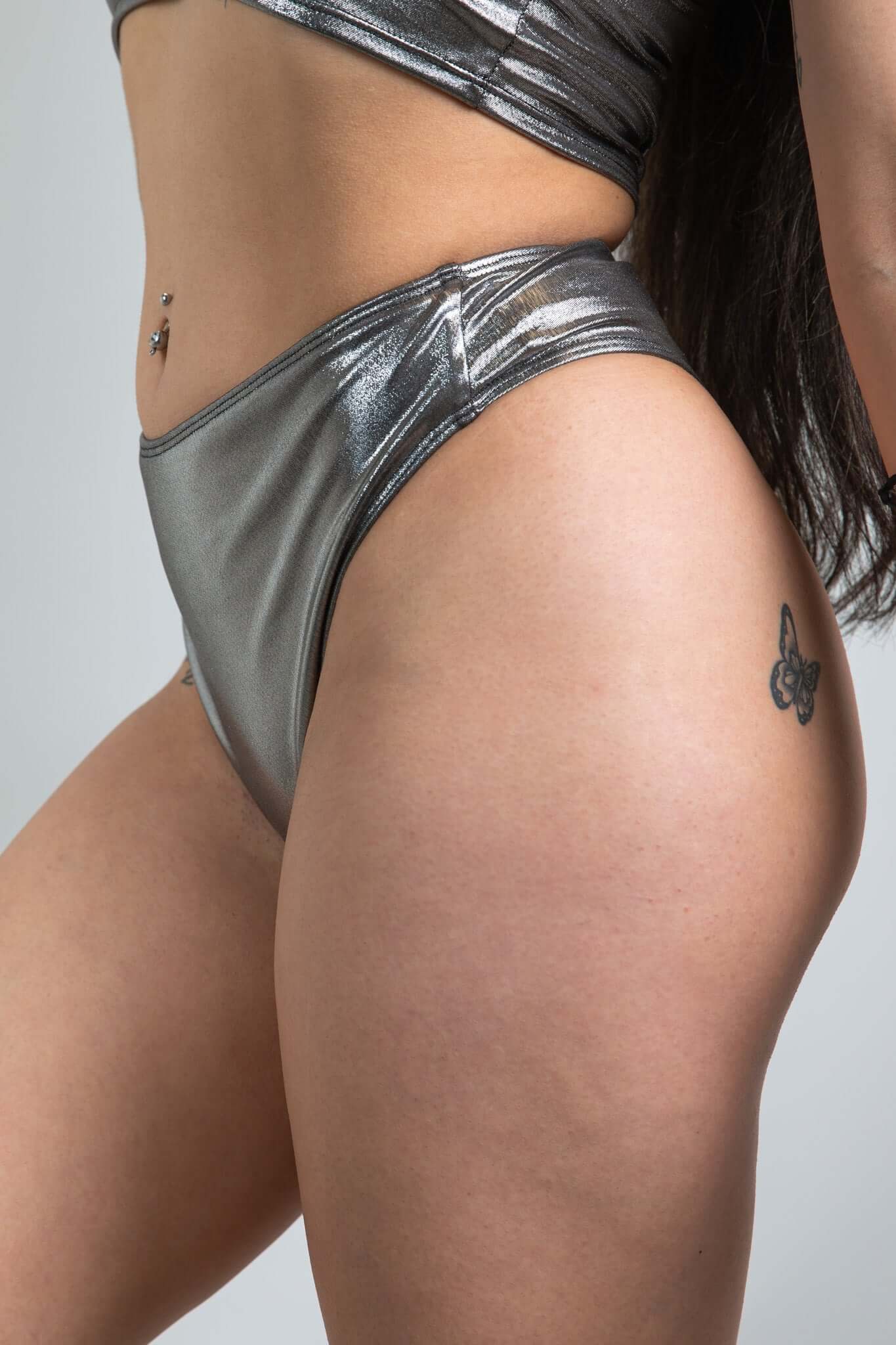 An up close photo of a woman wearing chrome bikini bottoms with a matching crop top. She is facing to the left.