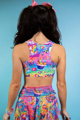 An up close photo of a woman wearing a rainbow crop top with whimsical characters on it. She is facing away from the camera.