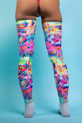A girl's legs, wearing rainbow leg sleeves with whimsical characters on them. The sleeves go up to her mid thigh. She is facing away from the camera.