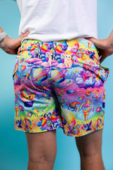 An up close photo of a man wearing rainbow shorts with whimsical characters and a white t-shirt. He is facing away from the camera.
