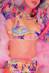 A woman lying on a cloud wearing a rainbow crop top with a large cutout in the middle and matching bikini bottoms.