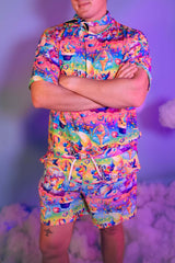 An up close photo of a man wearing a rainbow t-shirt with whimsical characters on it and matching shorts.