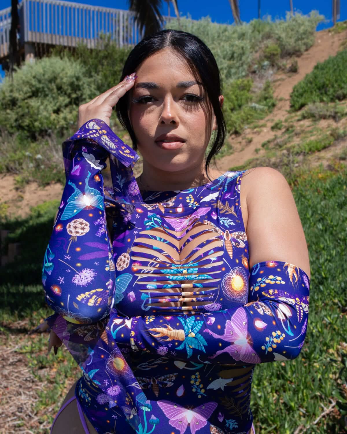 Model wearing Lucent Spellcaster Arm Sleeves with a vibrant mushroom and moth print in a green outdoor setting.