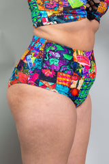 A woman wearing rainbow patchwork bikini bottoms and a matching crop top. She is facing to the right.