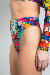 An up close photo of a girl wearing a high waisted rainbow patchwork bikini bottom with a matching crop top. She is facing to the left.
