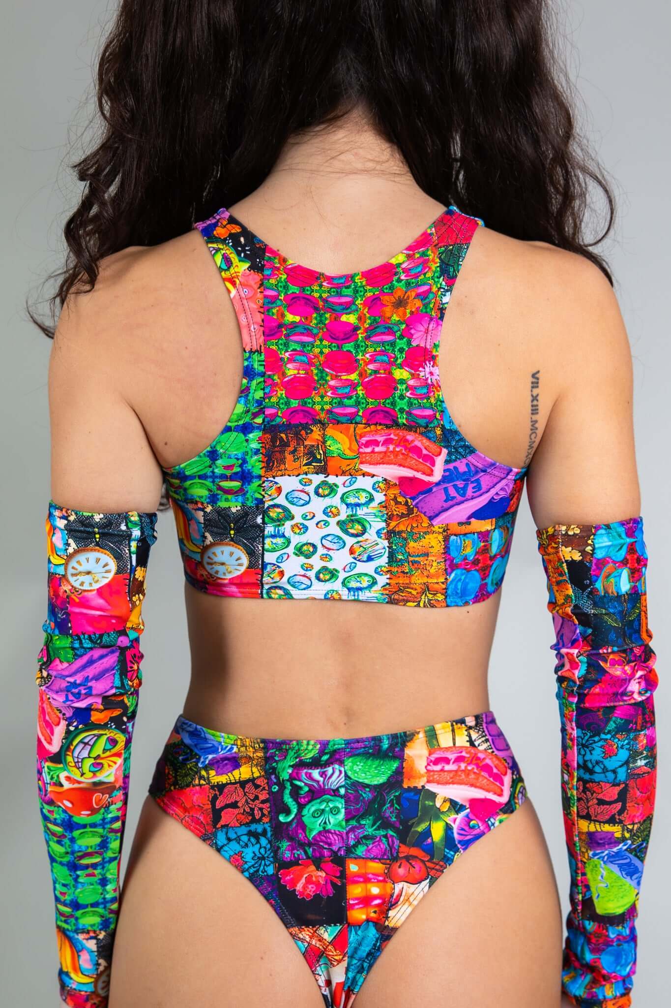 An up close photo of a woman wearing a rainbow patchwork crop top. She is facing away from the camera.