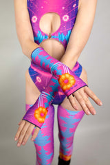 A photo of a woman wearing neon pink and blue rave gloves with a matching bodysuit.