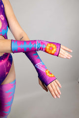 A photo of a woman wearing neon pink and blue rave gloves with a matching bodysuit. Her arms cross at the wrist.
