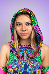 A photo of a girl looking at the camera with a soft smile wearing a rainbow stained glass printed hood and a matching bodysuit.