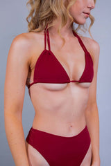 Close-up of a woman wearing a strappy, deep red bikini top by Freedom Rave Wear, paired with matching high-waisted bottoms