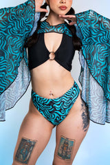 A woman wearing blue and black swirled bikini bottoms with matching mesh bell sleeves and a black crop top.