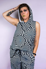 A person with unique makeup wearing a black and white geometric printed hooded tank top and matching pants.
