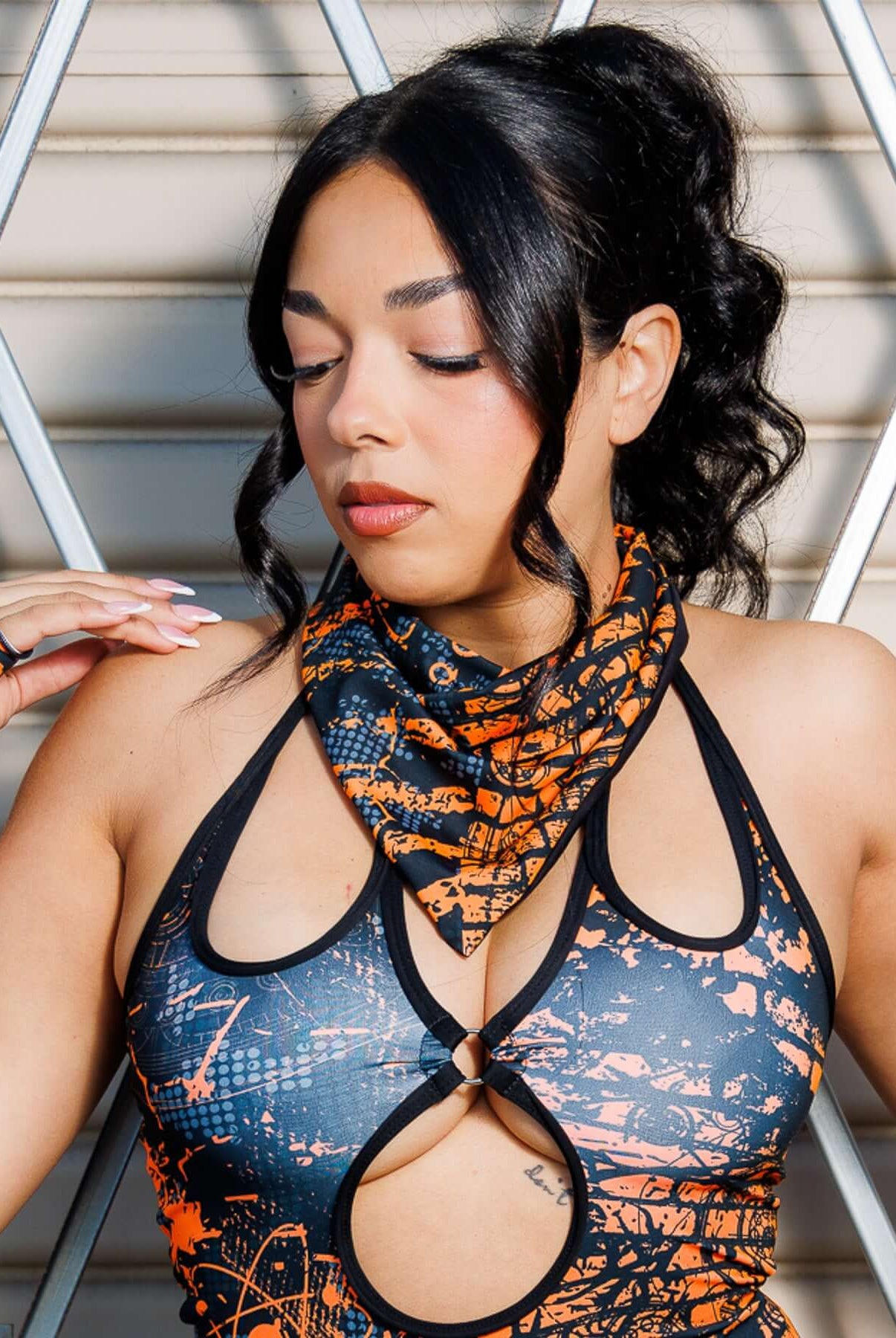 Woman wearing Atomic Bandana in orange and black with post-apocalyptic design, styled as a neck scarf for festival fashion.