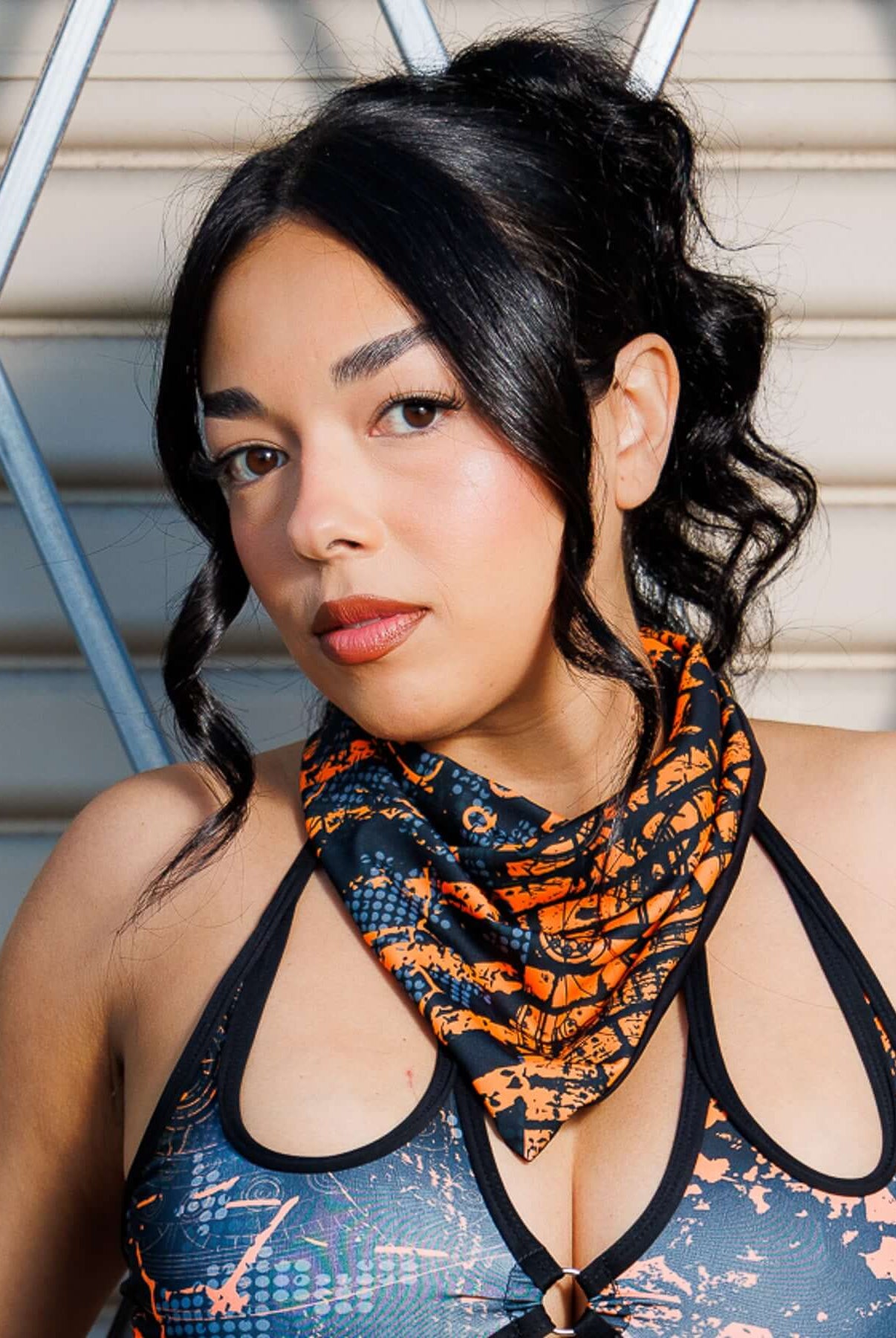 Model wearing Atomic Bandana in bold orange and black tones, styled as a neck scarf for a post-apocalyptic festival look.