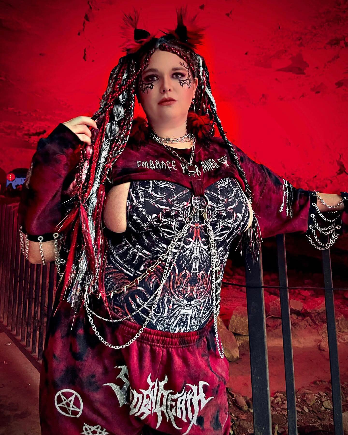 edgy festival outfit with chains and dark hairstyle against a vibrant red background, perfect for rave lovers.