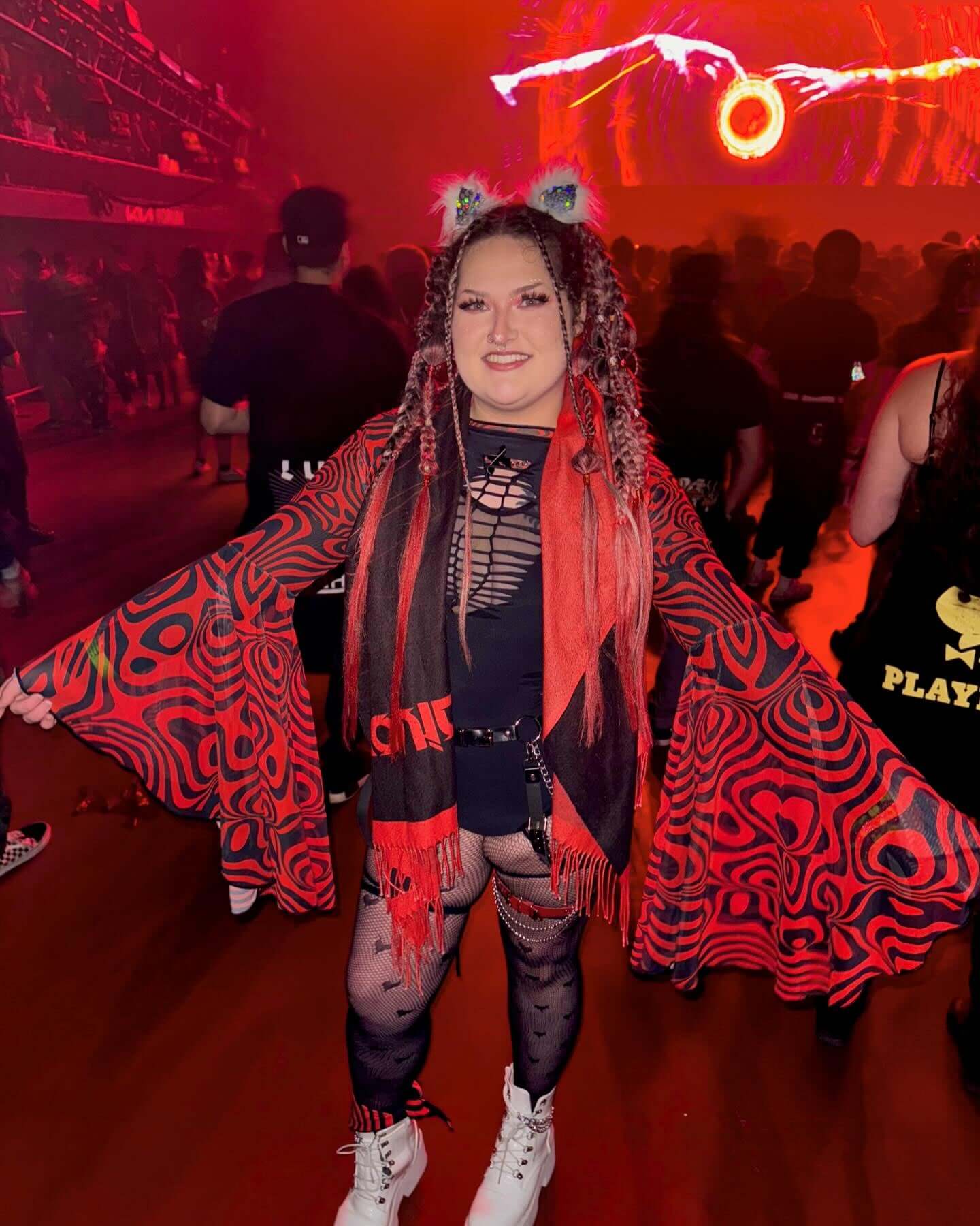 Vibrant rave enthusiast in a dynamic red and black patterned outfit, complete with layered shawls and playful accessories, celebrating at a festival