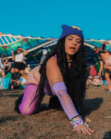 raver in a purple rave outfit with slit detailing kneels on the floor showing off the accessories of her outfit