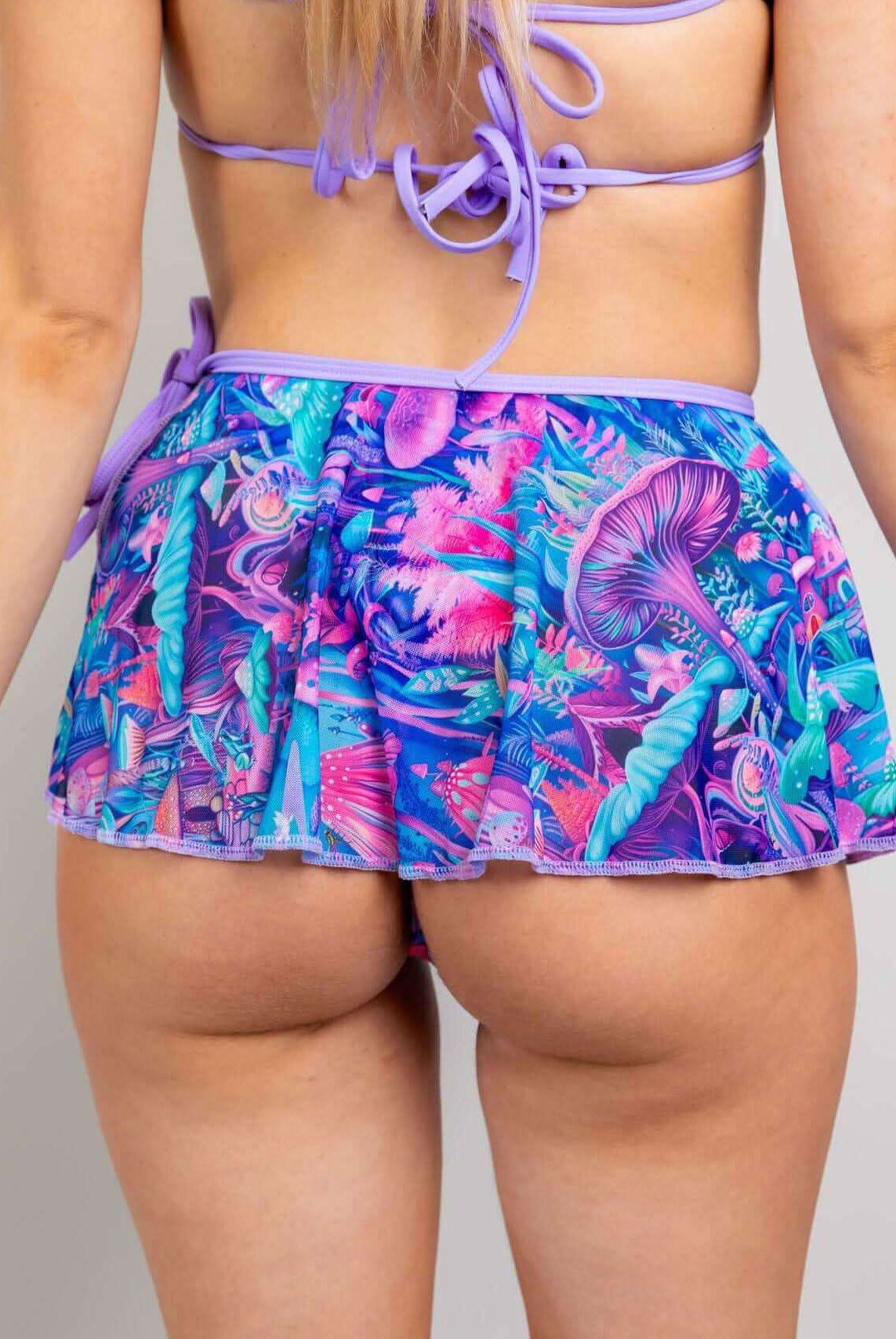 Back view of a model wearing a vibrant purple and teal fairycore mesh skirt, showcasing a tropical design.