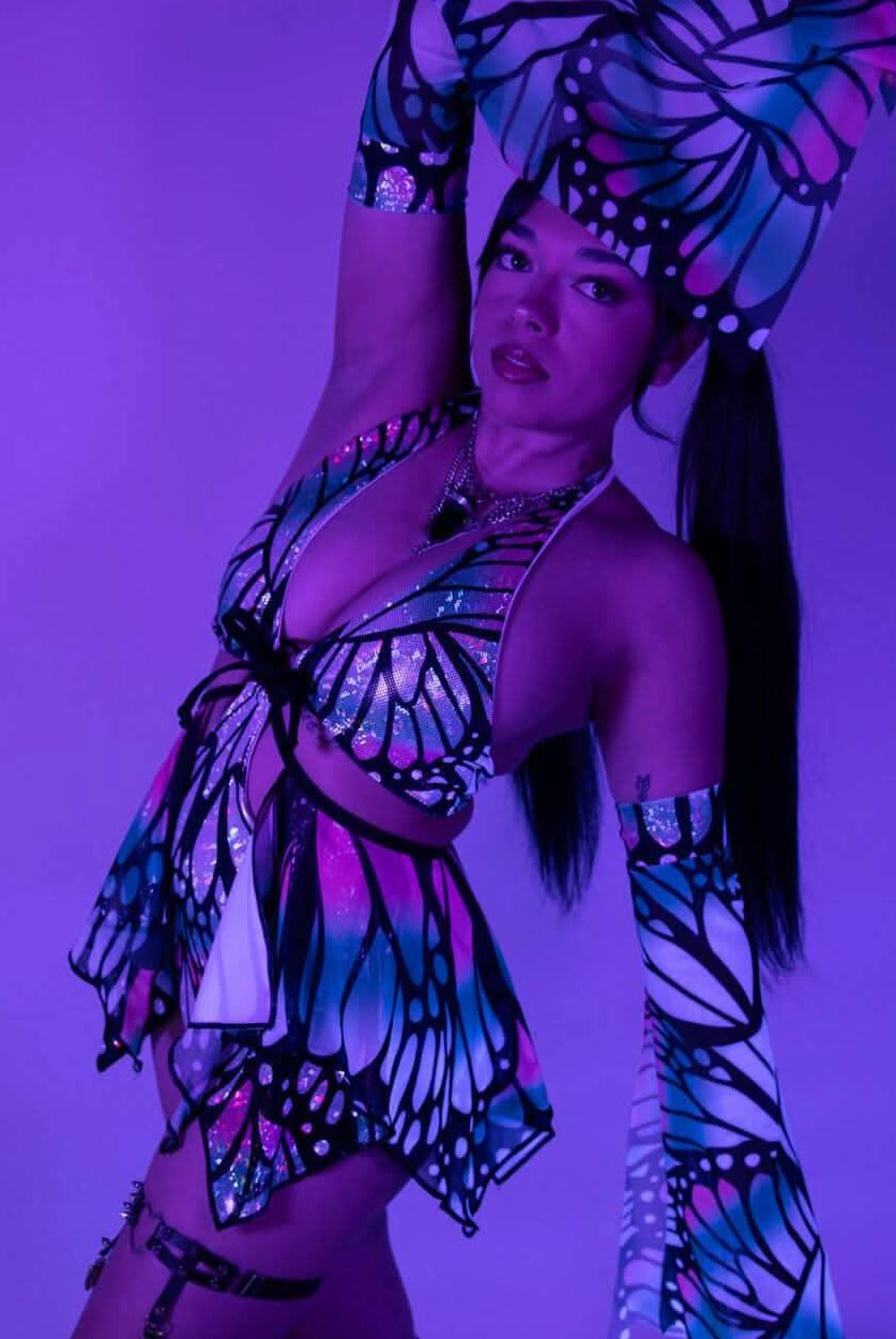 Model poses in a colorful butterfly print outfit, showcasing rave-inspired fashion with vibrant colors and fun accessories.
