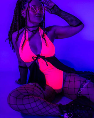 Neon-lit pose of the Hot Pink O-Ring Bodysuit, highlighting its glowing effect under blacklight.
