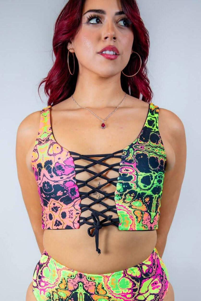 Model wearing the Intensity Lace Up Top, a UV reactive lace-up crop top with colorful skull design, perfect for rave outfits.
