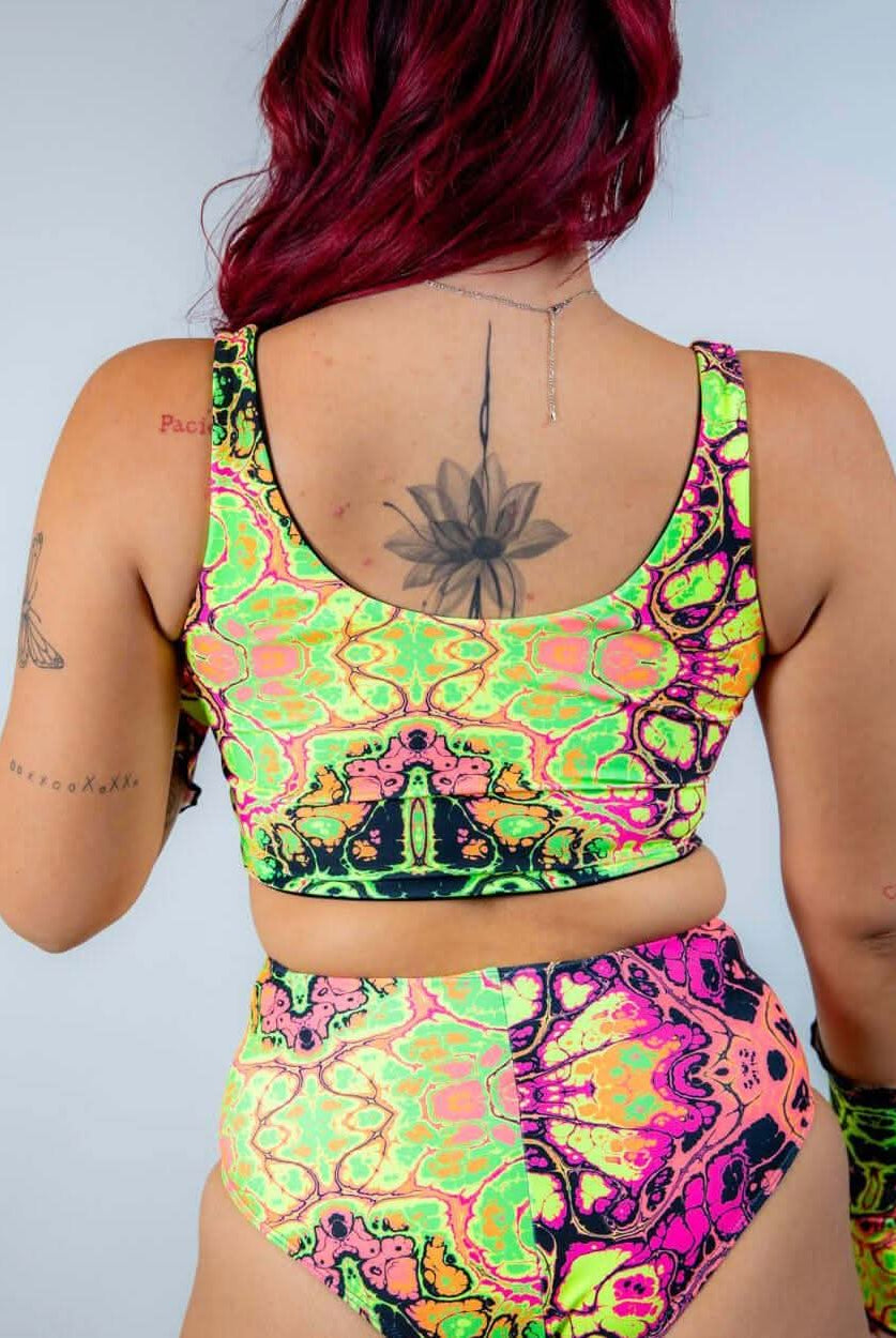 Back view of a model wearing a bright, UV reactive crop top and high-waisted bottom, perfect for rave outfits.