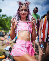 raver shines in neon pink and white rave outfit with fluffy ear accessories standing admist a festival crowd