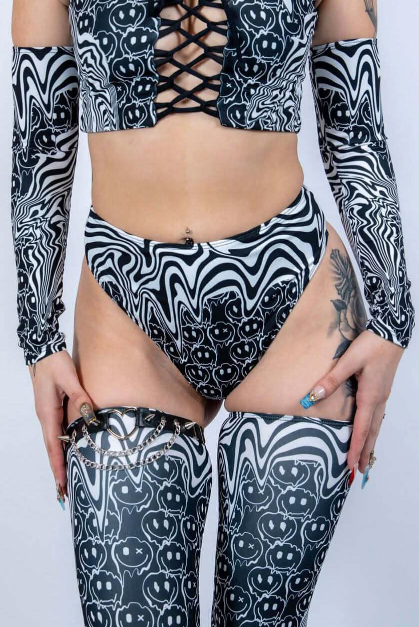 Model wearing the Meltdown High Waisted Thong with matching pieces, highlighting the high-rise waist and trippy smiley design.