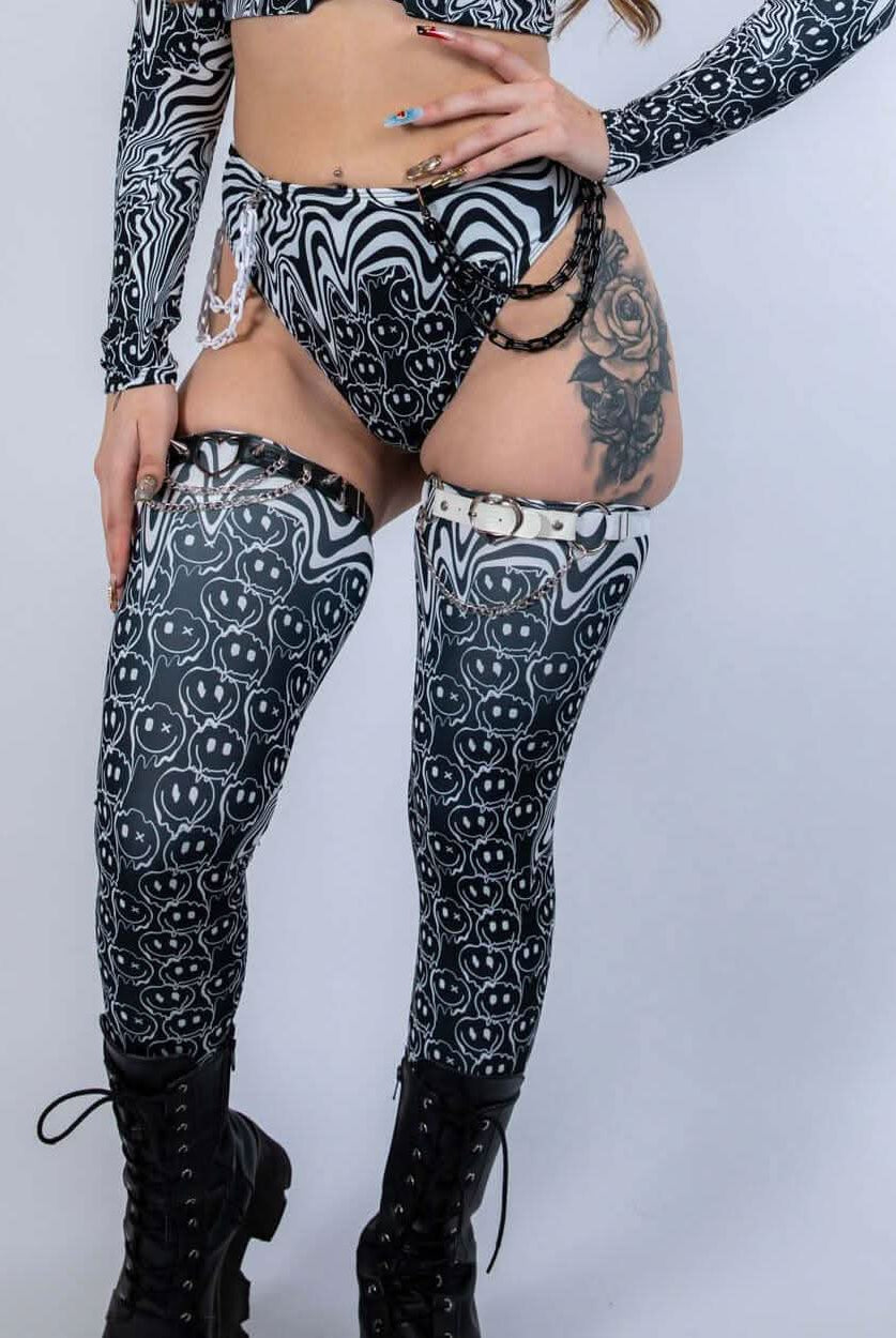 Model wearing Meltdown Leg Sleeves in a front-facing pose with matching ravewear, highlighting the melty smiley design and high-boot coverage.