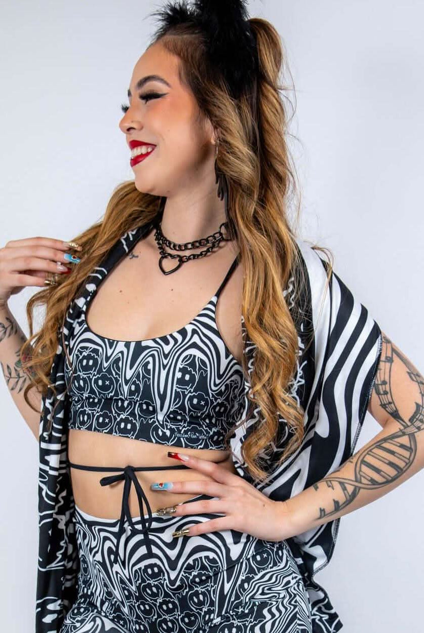 Model wearing the Meltdown Lush Top with one arm raised, showcasing the halter-style neckline and trippy smiley print.