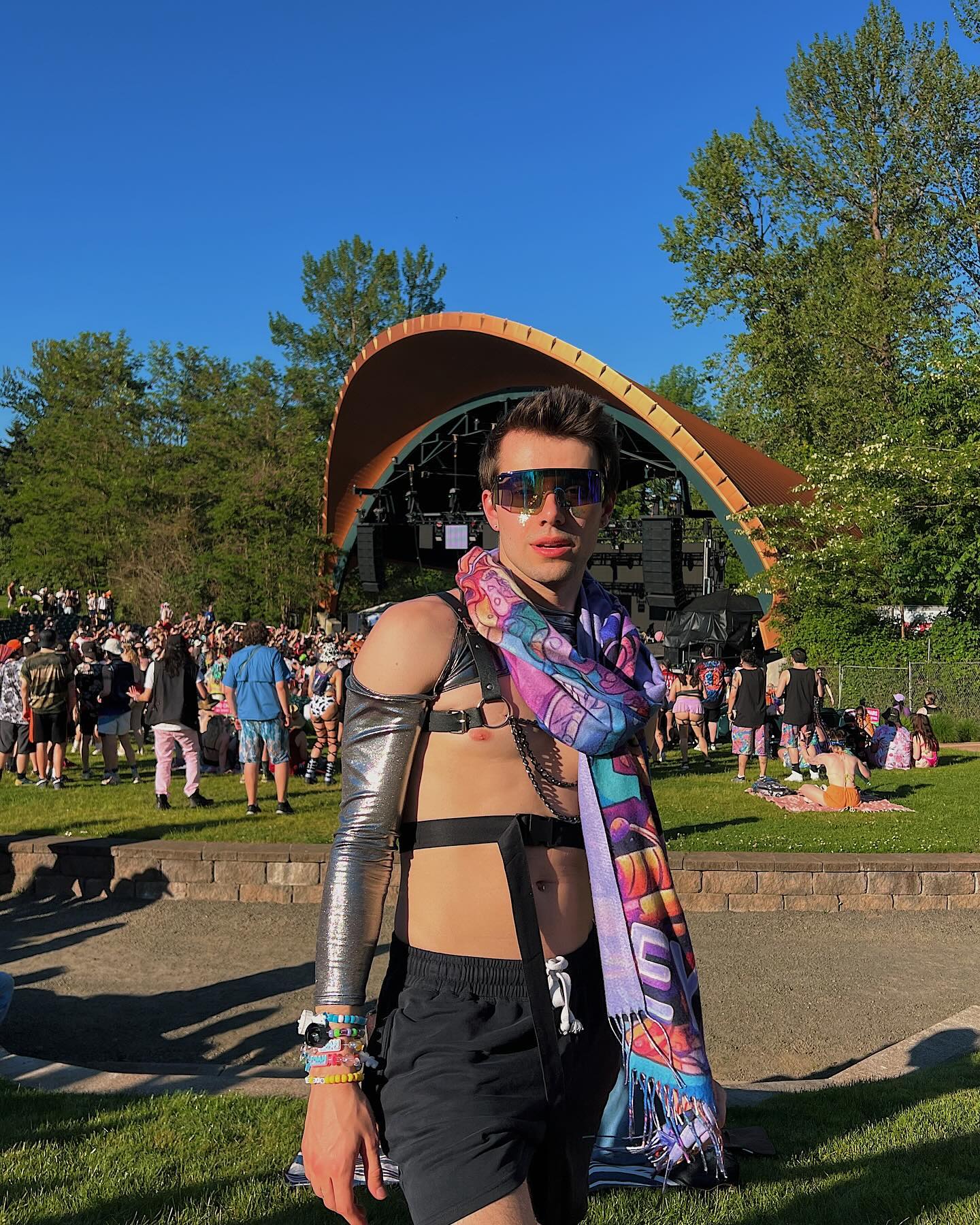 raver stand among crowd while wearing a rave outfit with chrome reflective arm sleeves and pashmina around neck exuding festival energy